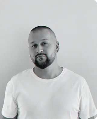 Man with a beard and shaved head, wearing a plain white t-shirt, looking at the camera.