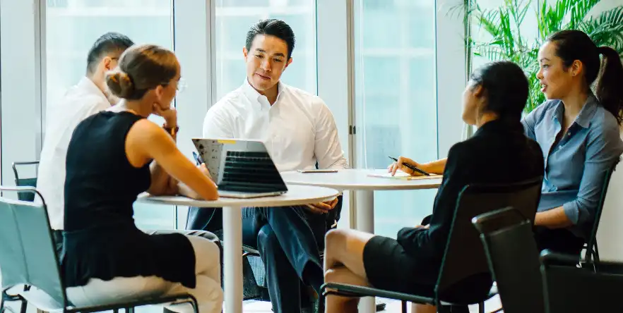 Office colleagues discussing work while seated around a table.