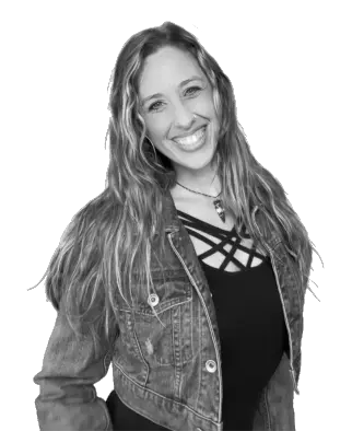 Woman smiling warmly, wearing a denim jacket over a crisscross patterned top.
