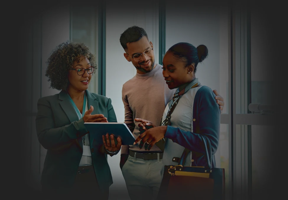 Three colleagues are discussing something on a tablet, smiling and engaged.