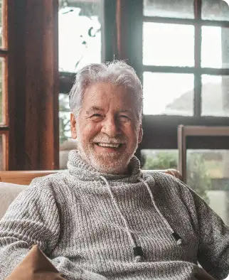 Elderly man with gray hair smiling, wearing a cozy sweater.